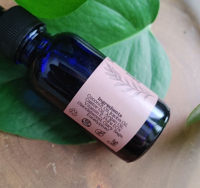 Blue glass bottle with a pink label on green leaves ingredient list