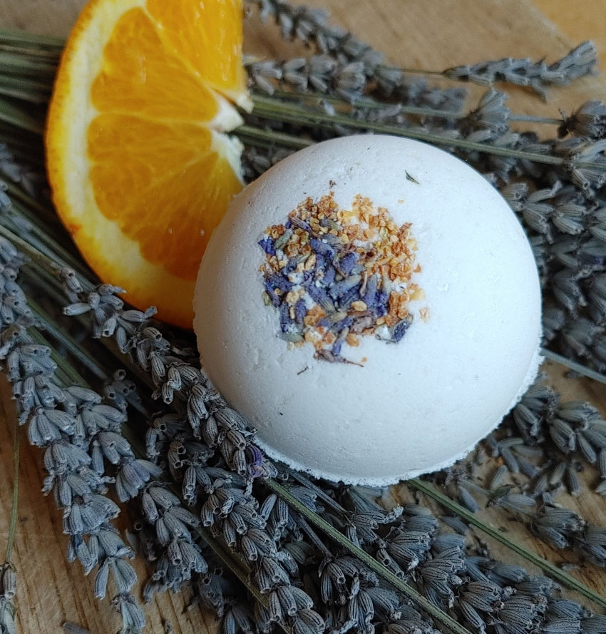 cedarwood lavender orange bath bomb with a fresh orange slice and dried lavender buds on a wood surface