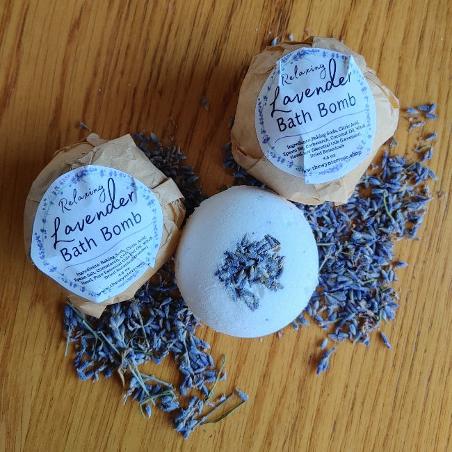 three lavender bath bombs together on a wooden surface surrounded by dried lavender buds