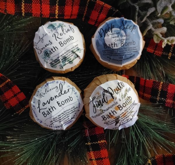 Four all natural bath bombs with labels on a decorative background with plaid ribbon and pine branches.
