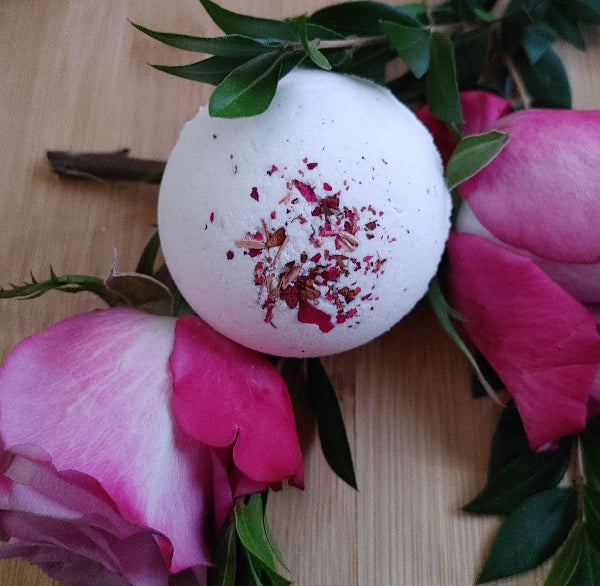 Dusty Rose Bath Bomb with rose and sandalwood essential oil blend for aromatherapy with fresh rose buds on a light wood surface