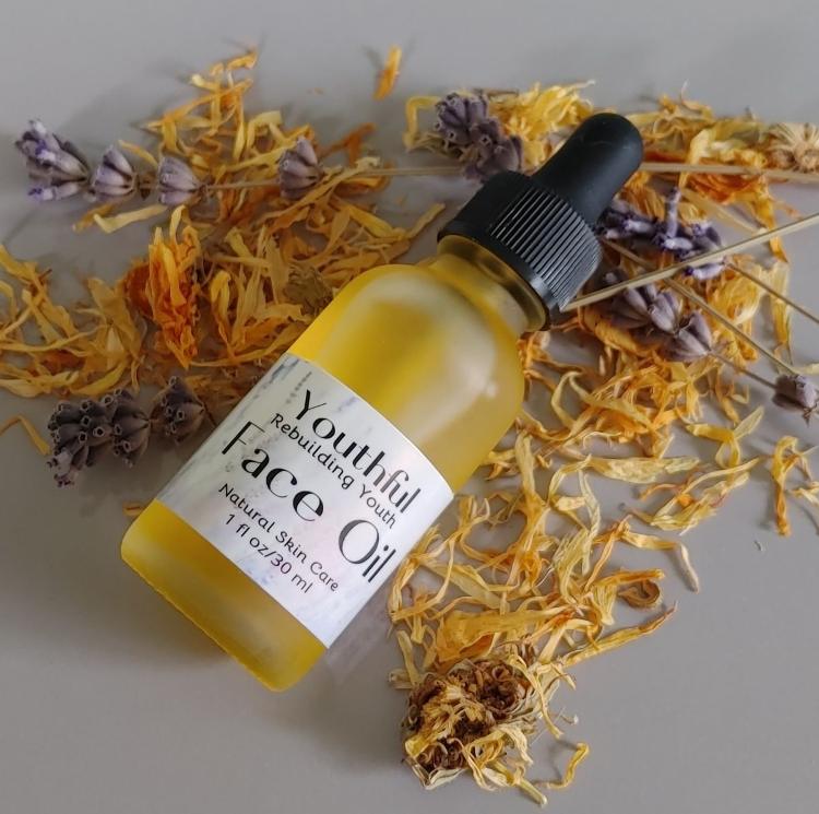 Bottle of Youthful Face Oil with a dropper on a surface with dried flowers and herbs.