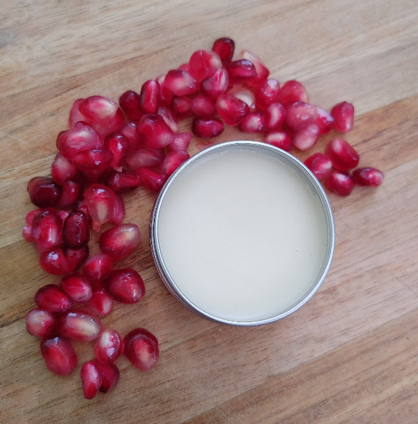 lip balm in a tin surrounded by fresh pomegrante seeds on a wooden board