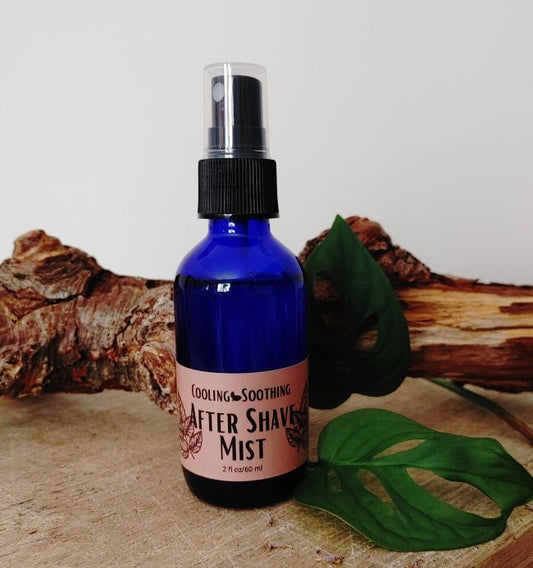 Blue spray bottle of after shave mist with a pink label on a wooden surface with leaves.