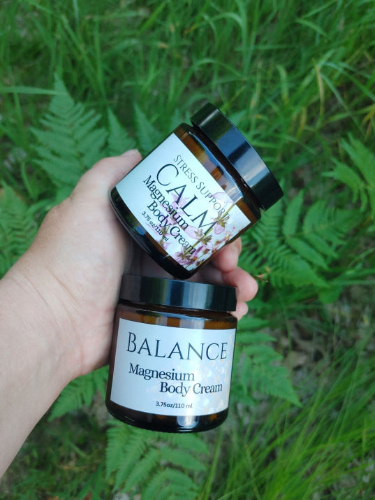 Two jars of plant based magnesium body cream held in a hand with a natural background