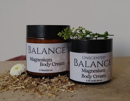 Two jars of Balance Magnesium Body Cream on a wooden surface with dried plants and flowers.