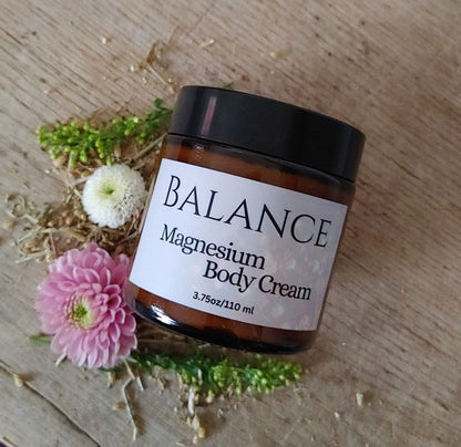 Jar of Balance Magnesium Body Cream on a wooden surface with flowers