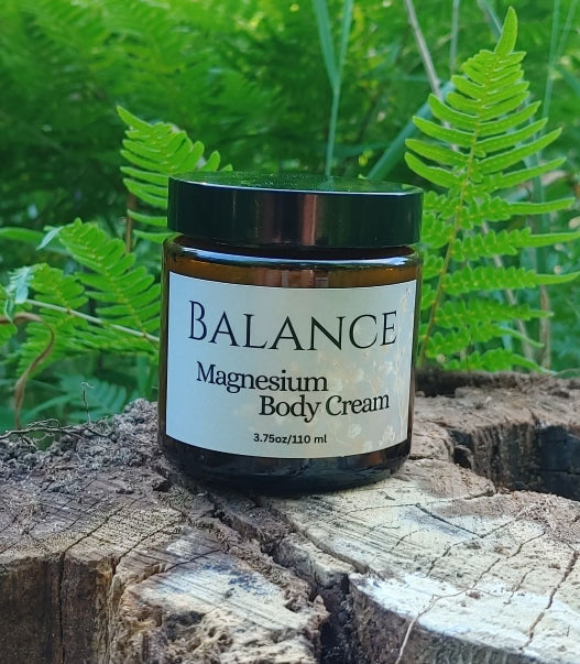 Jar of Balance Magnesium Body Cream on a wooden log with green ferns in the background