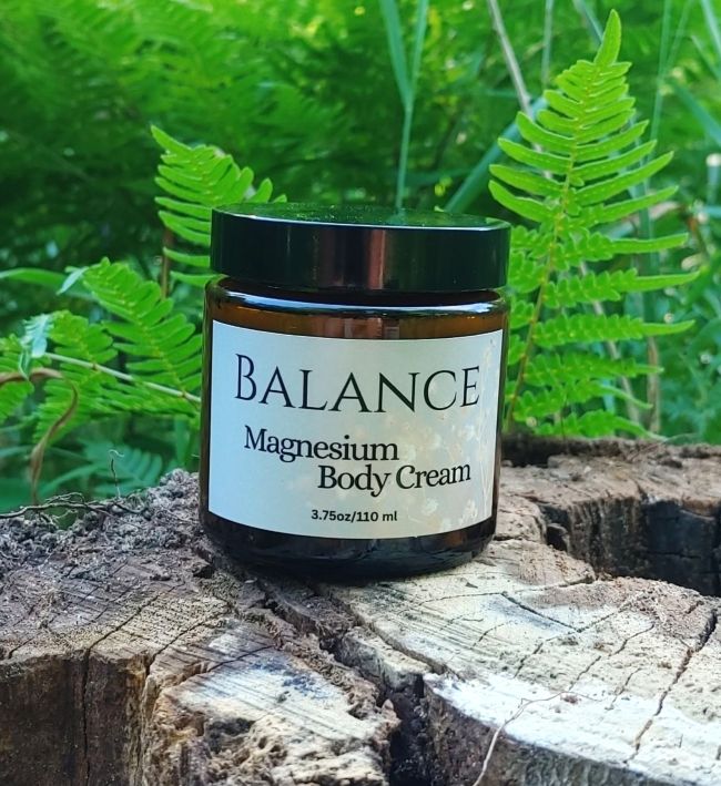 Jar of Balance Magnesium Body Cream on a wooden log with ferns in the background