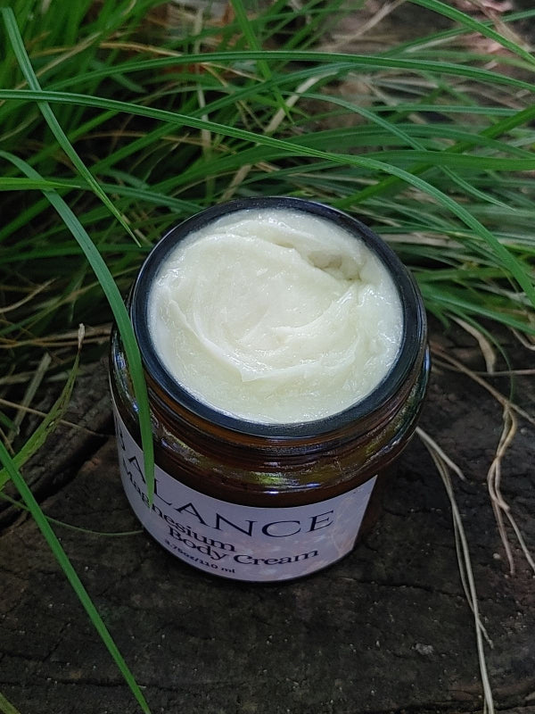 Jar of natural magnesium body cream on a wooden surface with grass in the background