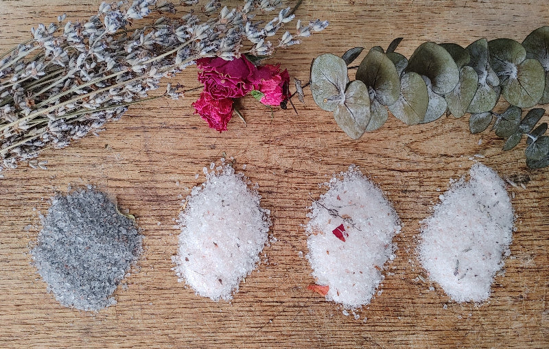 essential oil body soak and bath salt on a wooden surface with dried botanicals lavender and rose