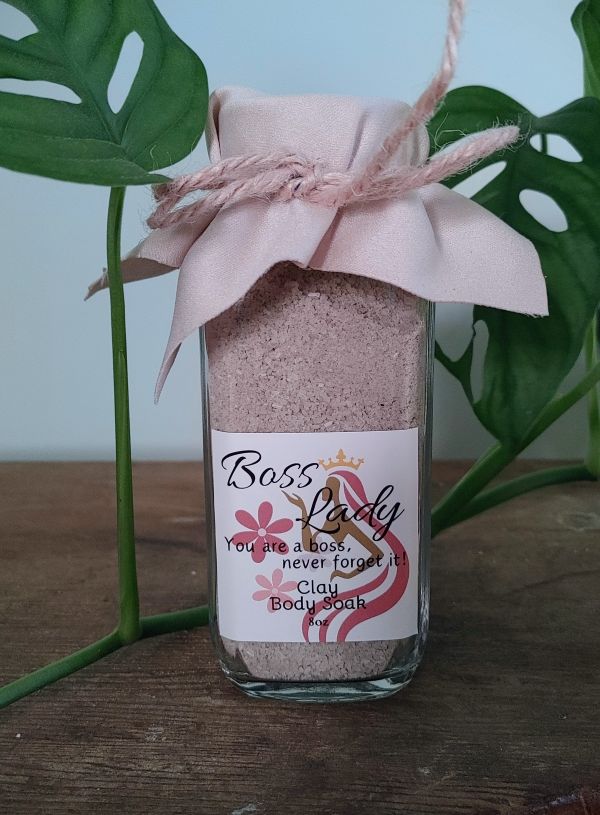 Bottle of 'Boss Lady' body soak with a decorative label and pink bow, set against a natural background. clay bath soak for radiant glowing skin