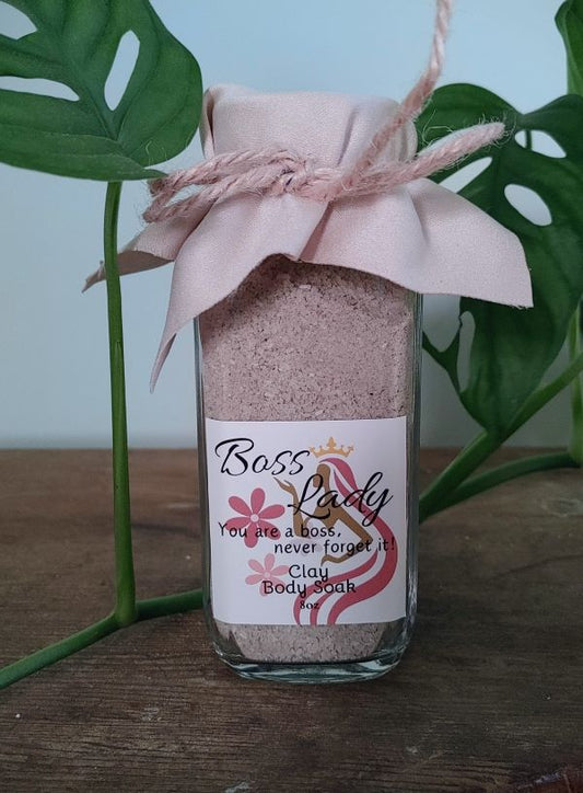 Bottle of 'Boss Lady' body soak with a decorative label and pink bow, set against a natural background. clay bath soak for radiant glowing skin