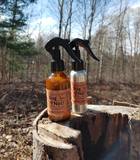 Two bottles of 'Bug & Not!' insect repellent on a wooden stump with a forest background.