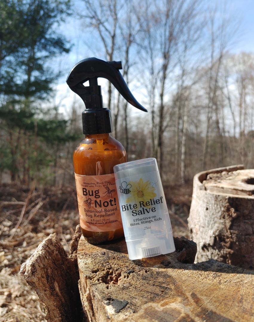 Two bottles of natural products, one spray bottle and one jar, on a wooden log with a forest background.