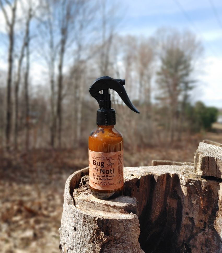 Bottle of 'Bug Not!' spray on a wooden stump with trees in the background