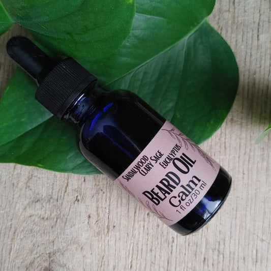 Bottle of beard oil with a label on a wooden surface with green leaves