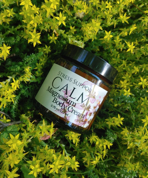 Jar of Calm magnesium body cream for stress and anxiety support displayed on a background of green foliage and yellow flowers