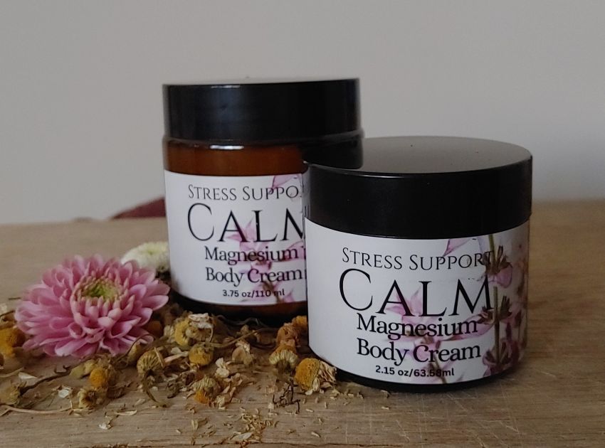 Two jars of Calm Magnesium Body Cream on a wooden surface with flowers and leaves.