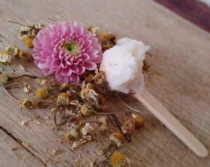 Magnesium body cream on a wooden spoon with  pink flower and dried botanicals on a wooden surface