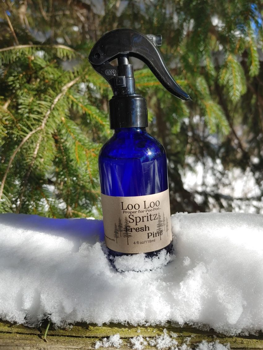 Blue spray bottle labeled 'Loo Loo Spritz' on a snowy surface with evergreen trees in the background