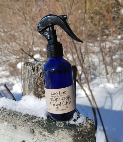 Blue spray bottle labeled 'Loo Loo Spritz Frosted Citrus' on a snowy surface with a blurred natural background.