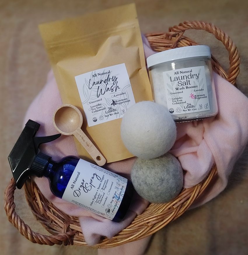Collection of natural laundry products including a spray bottle, laundry wash, dryer balls, and laundry salt in a basket.