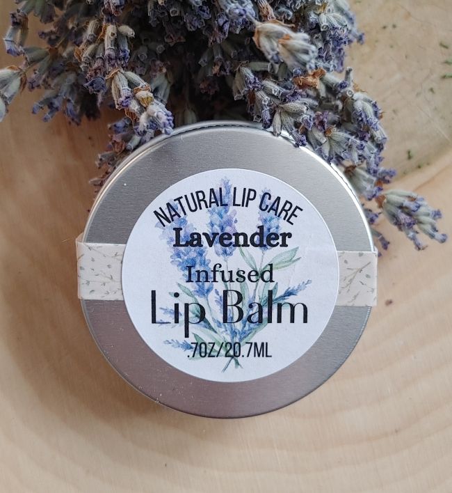 Lavender infused lip balm with a label on a wooden surface with lavender flowers.