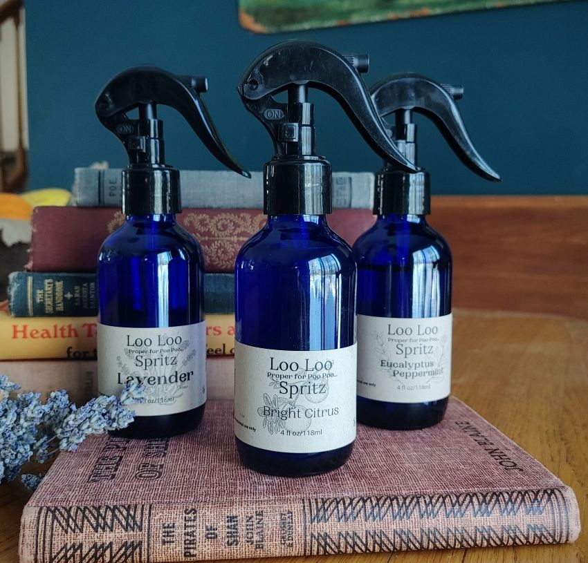 Three blue spray bottles labeled 'Loo Loo' on a wooden surface with books in the background.