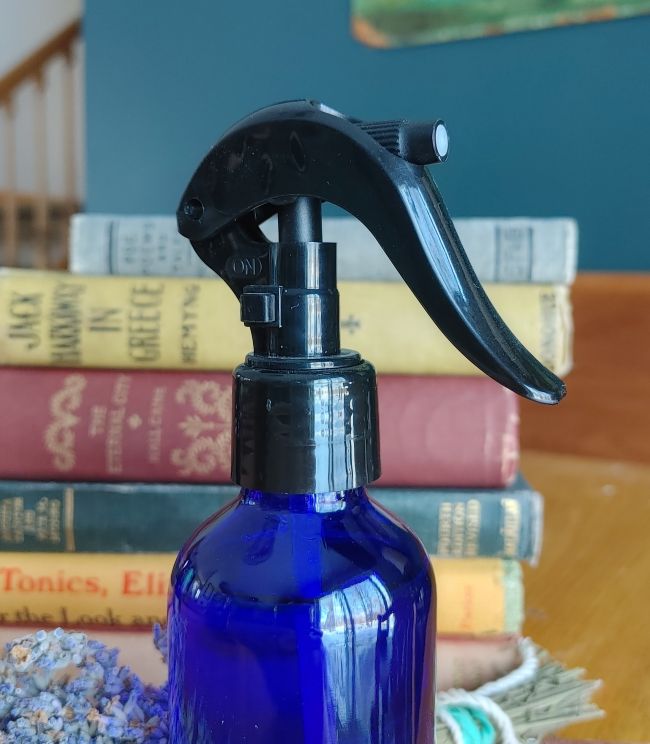 Blue spray bottle with black nozzle on a surface with books in the background