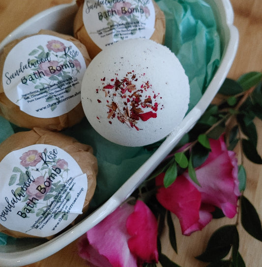 three sandalwood and rose essential oil bath bombs in a mini ceramic tub with fresh rose buds on the side