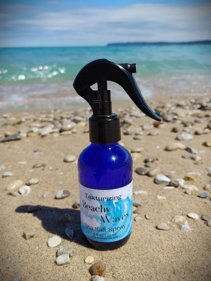 sea salt beachy waves hair spray for beach vibe mermaid hair housed in a blue glass bottle with black trigger spray top sandy michigan beach sleeping bear dunes backdrop