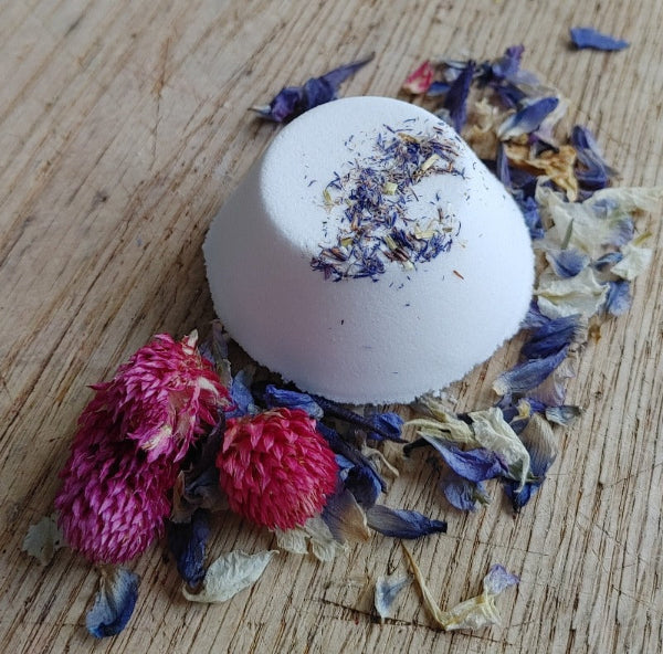 the wynter rose gardenia and ylang ylang aromatherapy shower steamer tab on a wooden background with purple and ink dried flowers