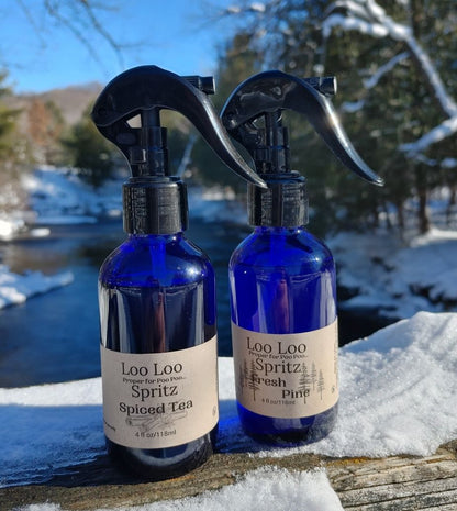 Two blue spray bottles labeled 'Loo Loo Spritz' on a snowy surface with a winter landscape in the background.