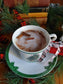 soy wax candle in holiday tea cup White mug with cinnamon stick on a green saucer, surrounded by Christmas decorations.