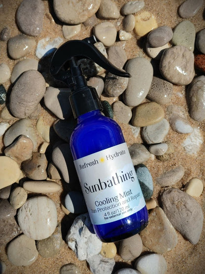 cooling mist refreshing hydrating peppermint cooling mist body spray witch hazel blue glass spray bottle on beach stone sand in michigan glen arbor