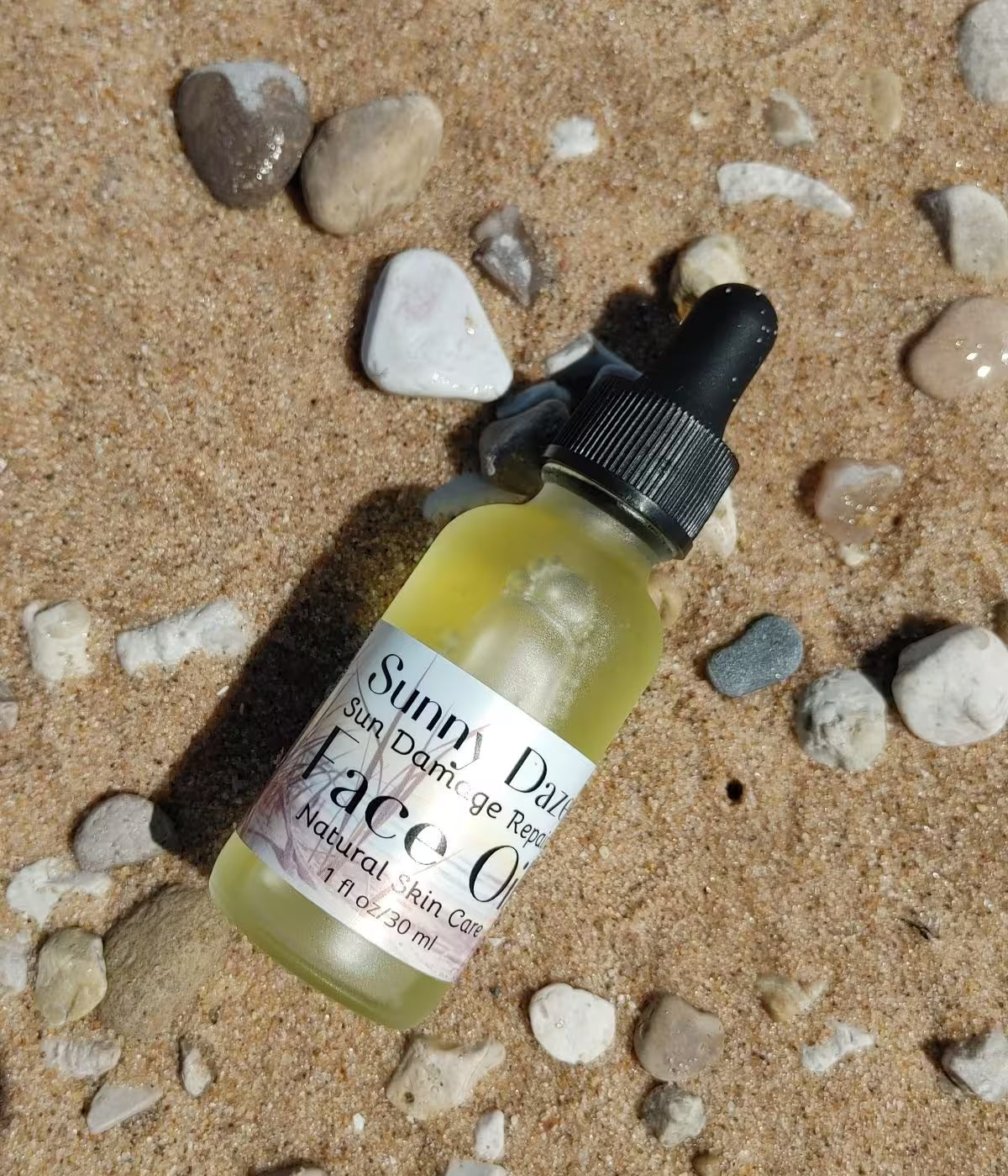 sun care sunny daze face oil laying on beach sand with small pebbles