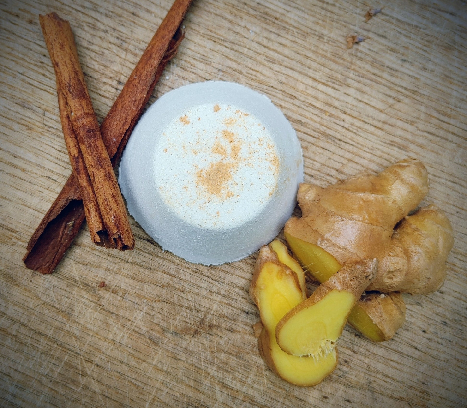 ginger vanilla cinnamon shower steamer tablet with cinnamon sticks and ginger on a wooden surface